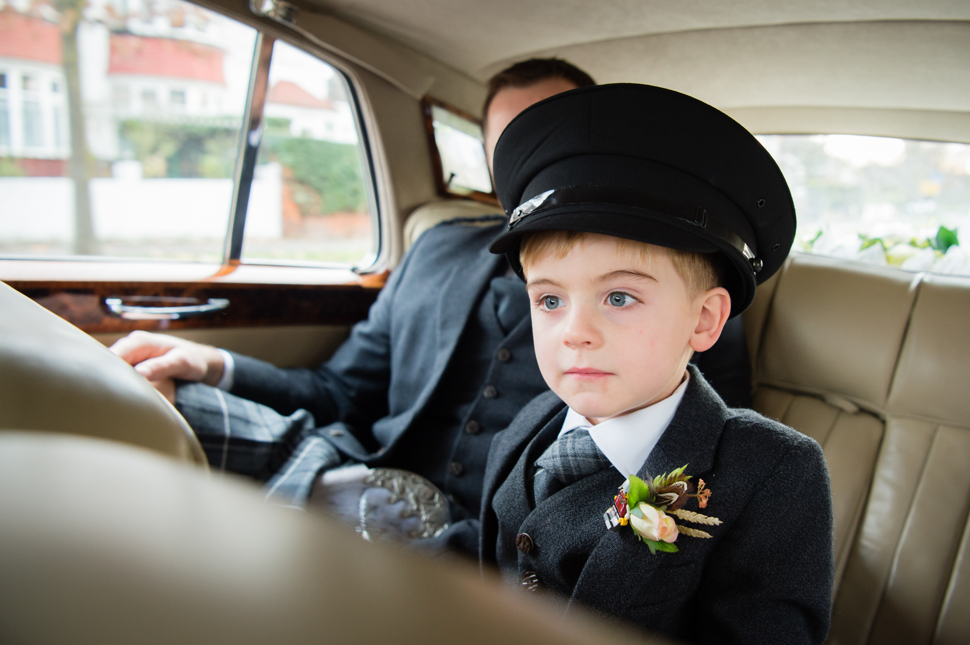 A boy wearing a chauffeur's hat in the back of a classic car